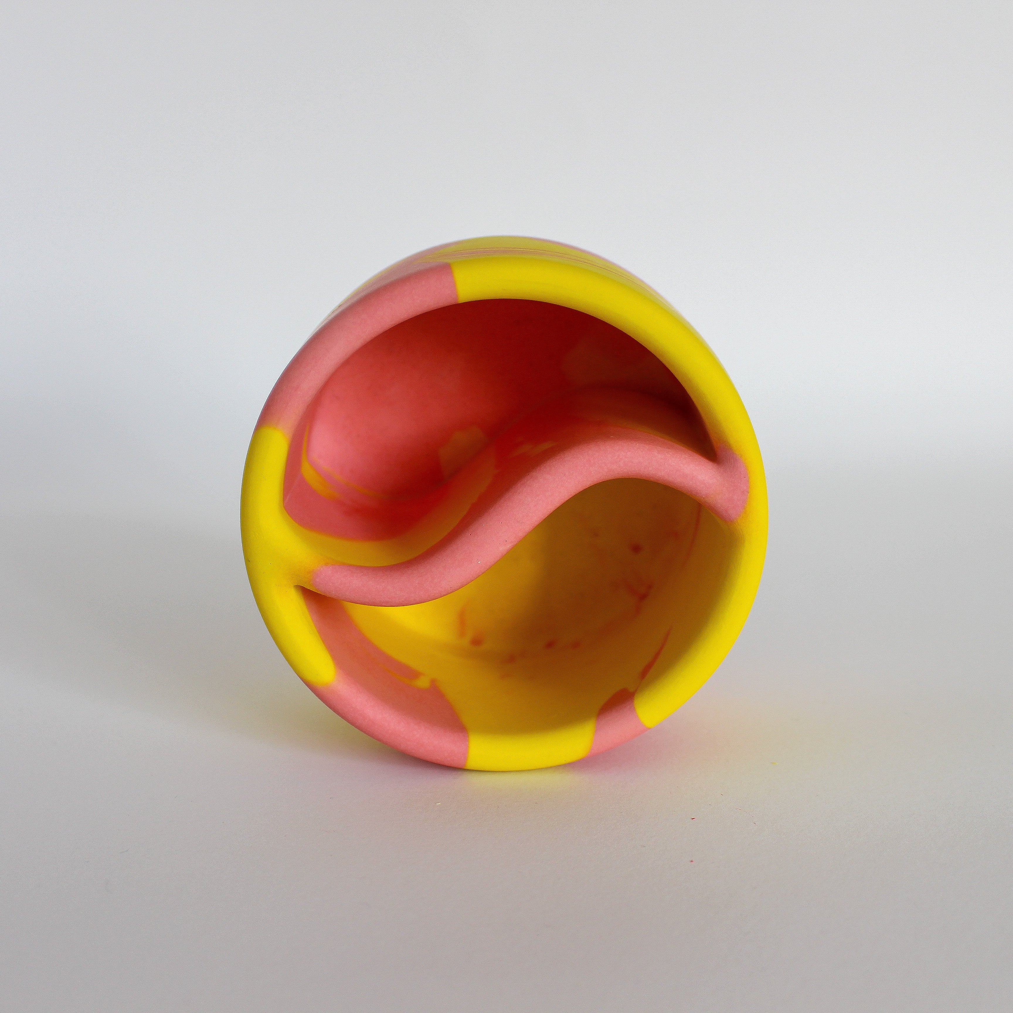Top view of a handmade decorative bowl with a marbled pink and yellow pattern, shaped like a Yin Yang symbol with two compartments.